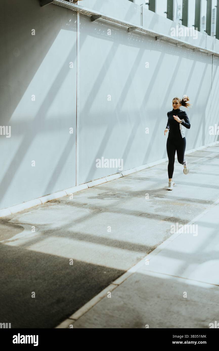 Un passionné de fitness descend une passerelle élégante, la lumière du soleil projette des ombres dynamiques sur le sol alors que la ville prend vie. Banque D'Images