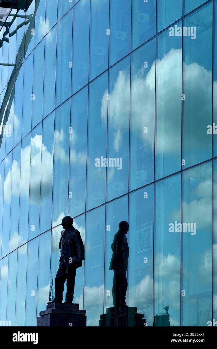 Statue de Sir Matt Busby au stade de football Old Trafford. Statue et reflet avec des nuages et le ciel bleu reflété dans les fenêtres de l'avant du stade. Manthorax - Image de stock capturée avec un smartphone