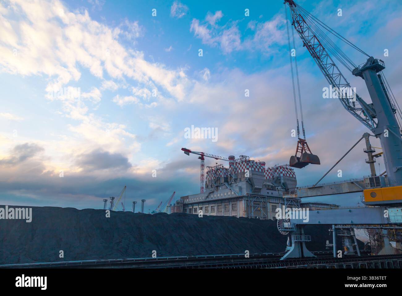 Le territoire d'une centrale à charbon, avec des grues, du charbon et un tuyau d'échappement au crépuscule. Banque D'Images