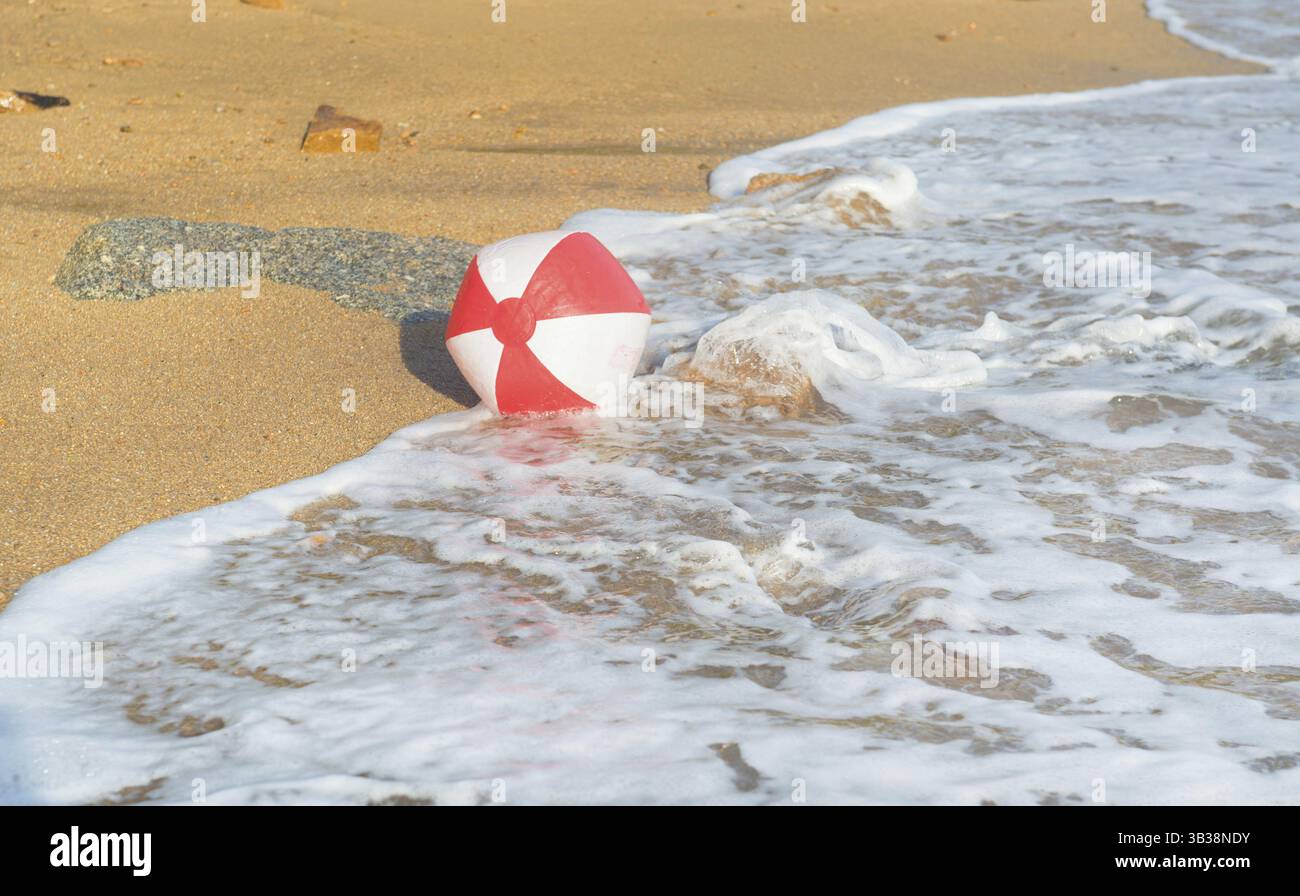 Ballon de plage rouge et blanc jouant avec les vagues et la mer à la plage Banque D'Images