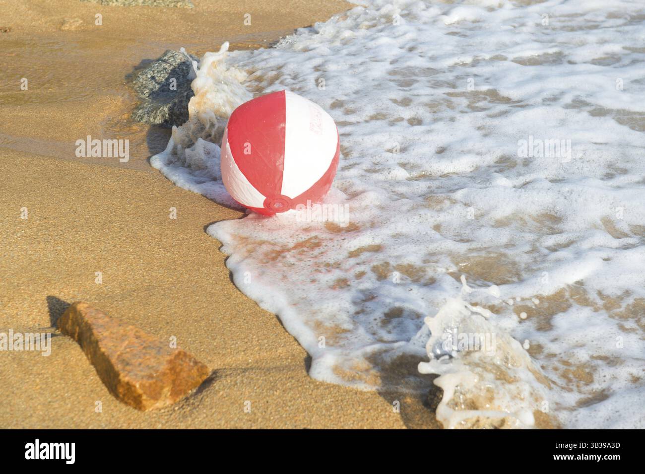 Ballon de plage rouge et blanc jouant avec les vagues et la mer à la plage Banque D'Images