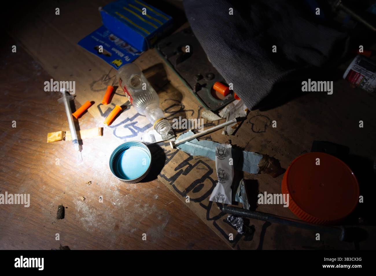 Les seringues usagées et les accessoires de drogue sont dispersés dans une pièce sombre, mettant en évidence la dépendance, la toxicomanie et les dangers de la crise des opioïdes. Banque D'Images