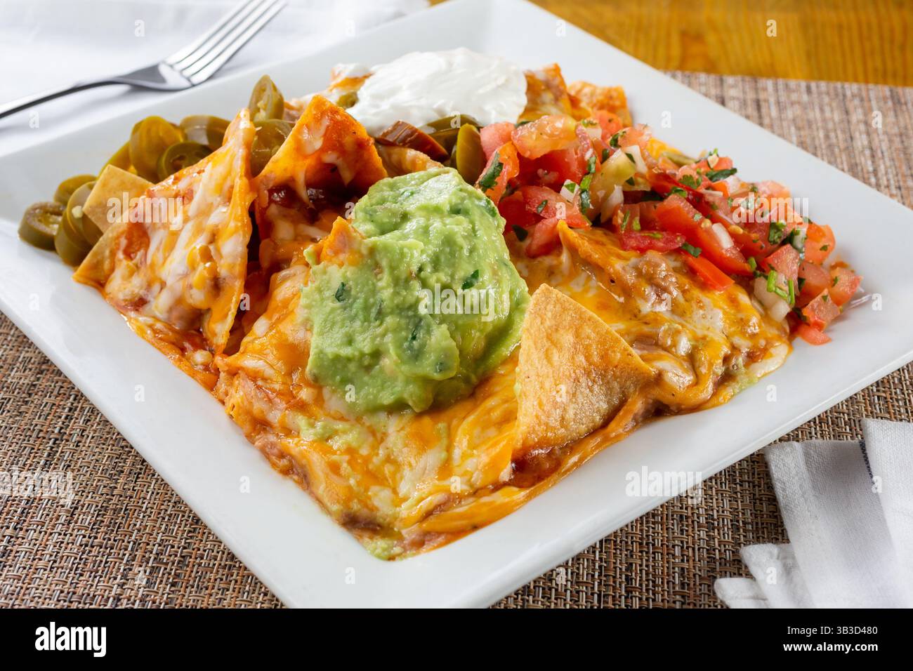 Une vue d'une assiette de nachos chargés, avec une grosse cuillère de guacamole. Banque D'Images