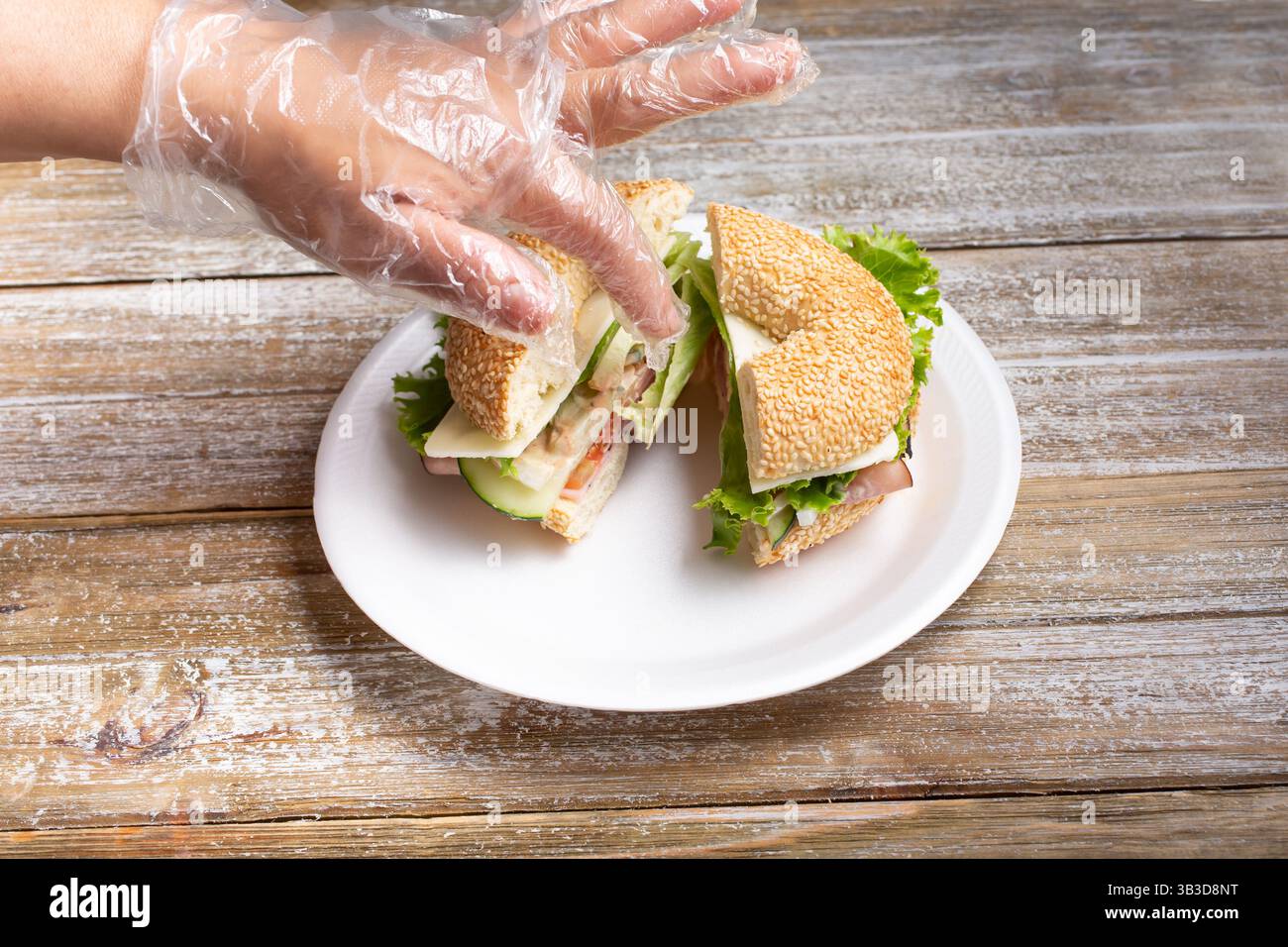 Une vue d'une main gantée préparant un sandwich bagel. Banque D'Images