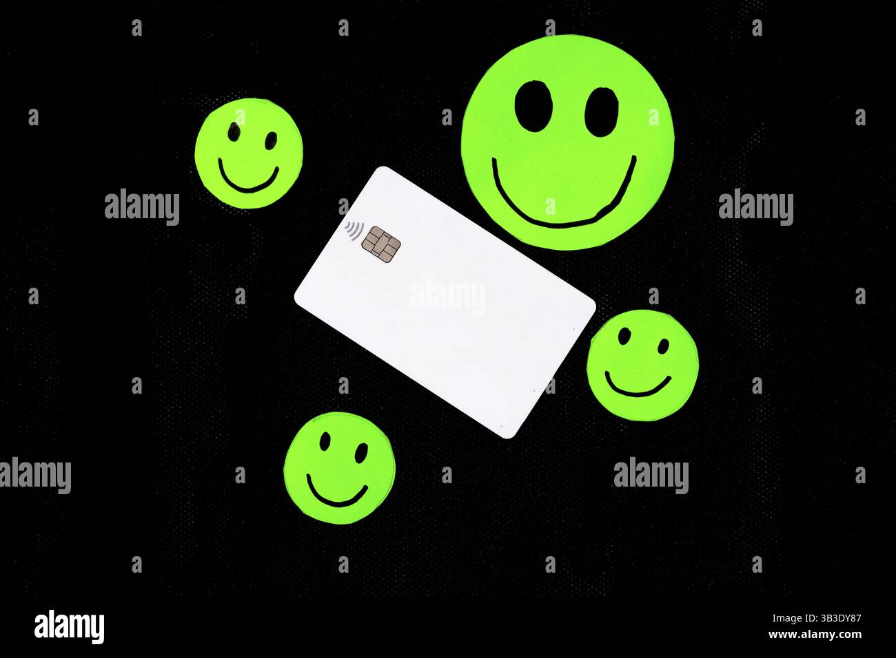 Une carte de crédit blanche entourée d'autocollants smiley vert fluo sur une surface sombre Banque D'Images