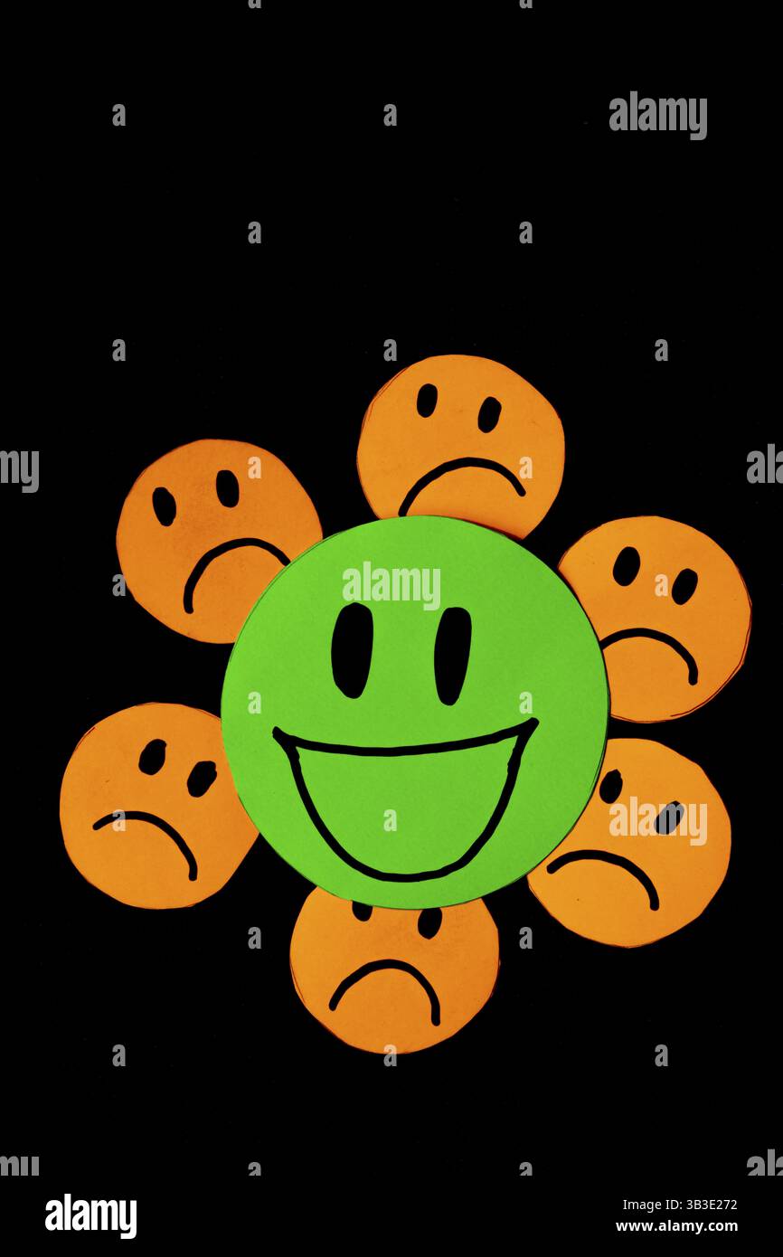 Image verticale de quelques émoticônes découpées dans du papier orange avec un visage triste entourant une grande émoticône verte avec un visage souriant. concept de mauvaise influence Banque D'Images