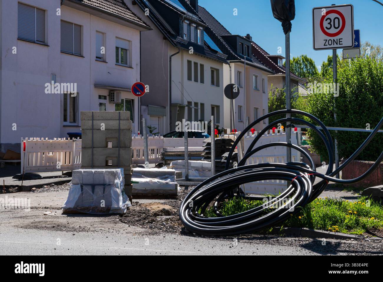 Les matériaux de construction ont été empilés et les câbles électriques ont été enroulés sur le sol dans une rue de la ville. Les bâtiments résidentiels bordent la rue sous un bleu clair Banque D'Images