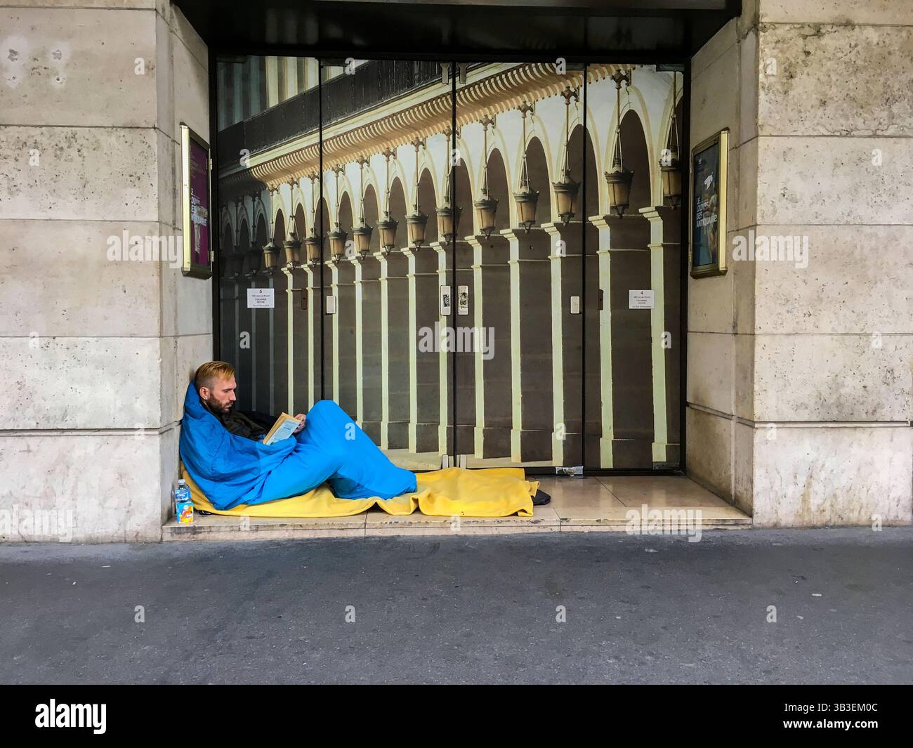Homme sans-abri avec des cheveux lisant son livre, tout en gardant au chaud dans son sac de couchage. Paris, France. Banque D'Images