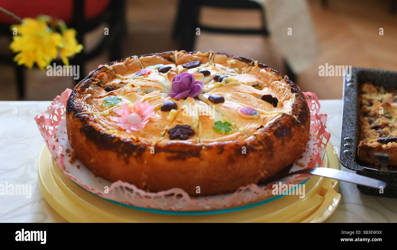 Gâteau aux pommes décoré avec du chocolat et des fleurs de sucre sur une table avec une autre pâtisserie cuite au four. Banque D'Images