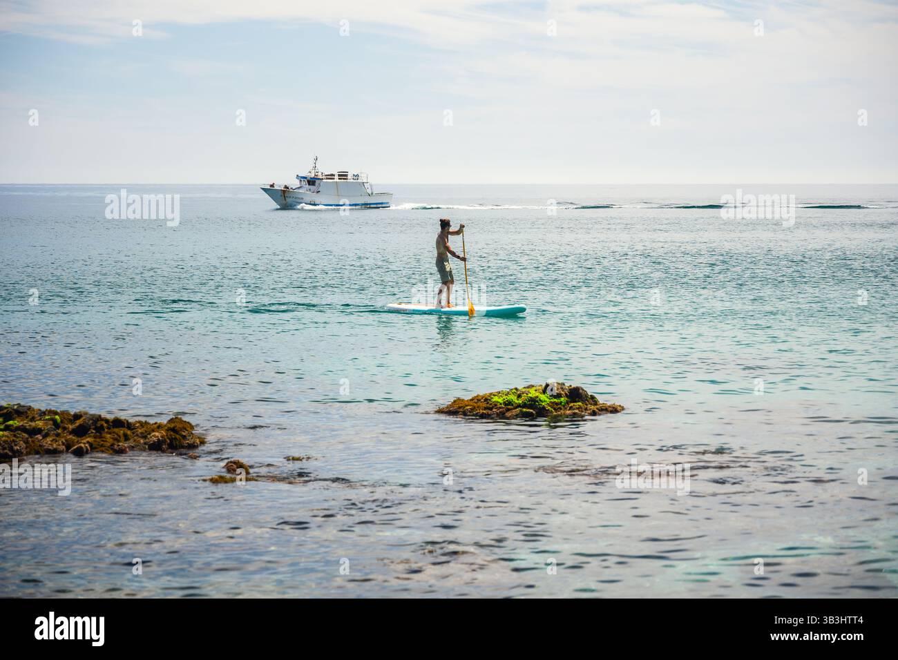 Cette photo côtière dynamique capture un homme en stand-up paddleboard sur des eaux bleues transparentes à Playa de los Muertos, avec une croisière en yacht blanc Banque D'Images