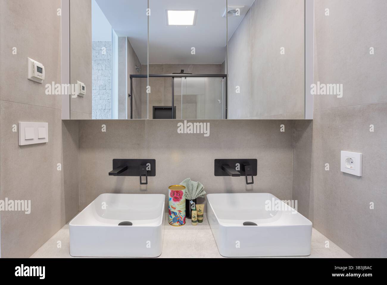 Salle de bains minimaliste lumineuse avec meuble-lavabo double, lavabos carrés, robinets muraux noir mat et armoires à miroirs. Banque D'Images
