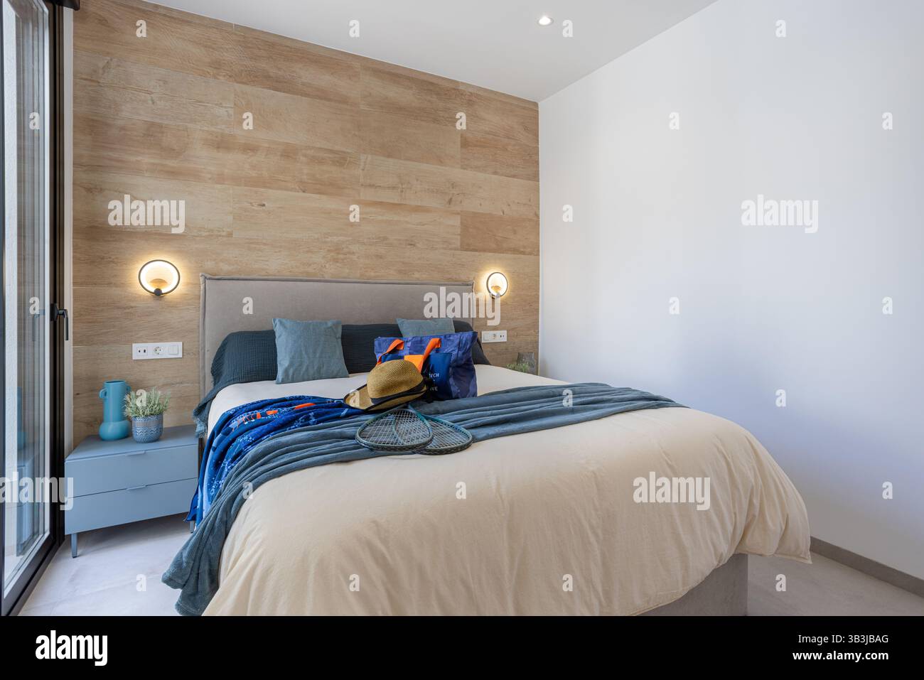 Chambre accueillante avec mur d'accent en bois naturel, literie confortable, textiles doux et grandes fenêtres permettant une lumière du jour abondante. Banque D'Images