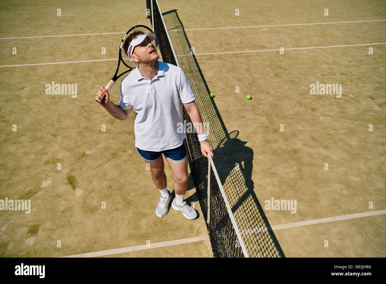 Un joueur confiant en vêtements de sport blancs se concentre sur le jeu tout en se tenant près du filet. Banque D'Images
