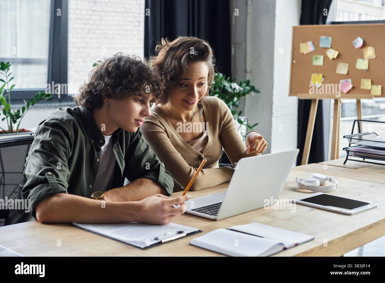 Deux collègues s'engagent avec enthousiasme sur un ordinateur portable tout en réfléchissant à des idées dans un bureau moderne. Banque D'Images