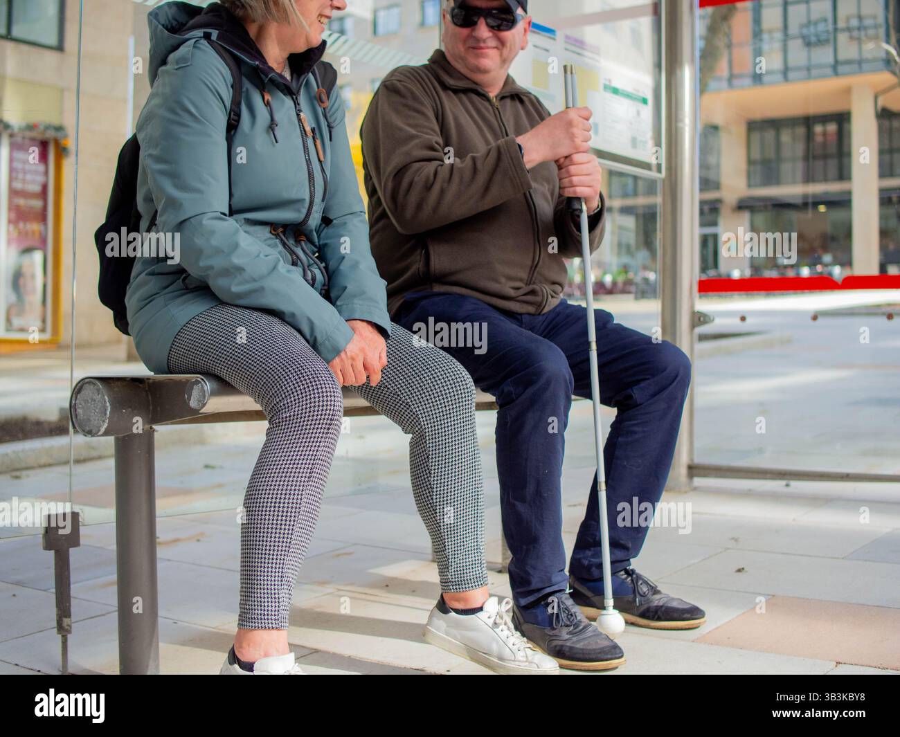 Un aveugle avec une canne blanche parle à une femme méconnaissable à l'arrêt de bus. Banque D'Images