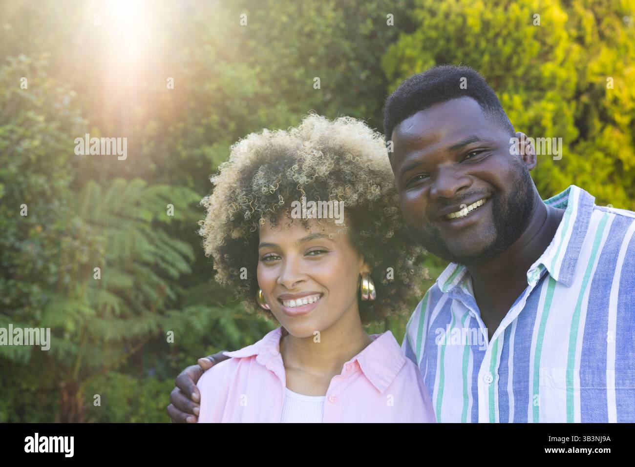 Couple souriant divers debout dans un jardin verdoyant luxuriant, avec le feuillage filtrant la lumière du soleil Banque D'Images