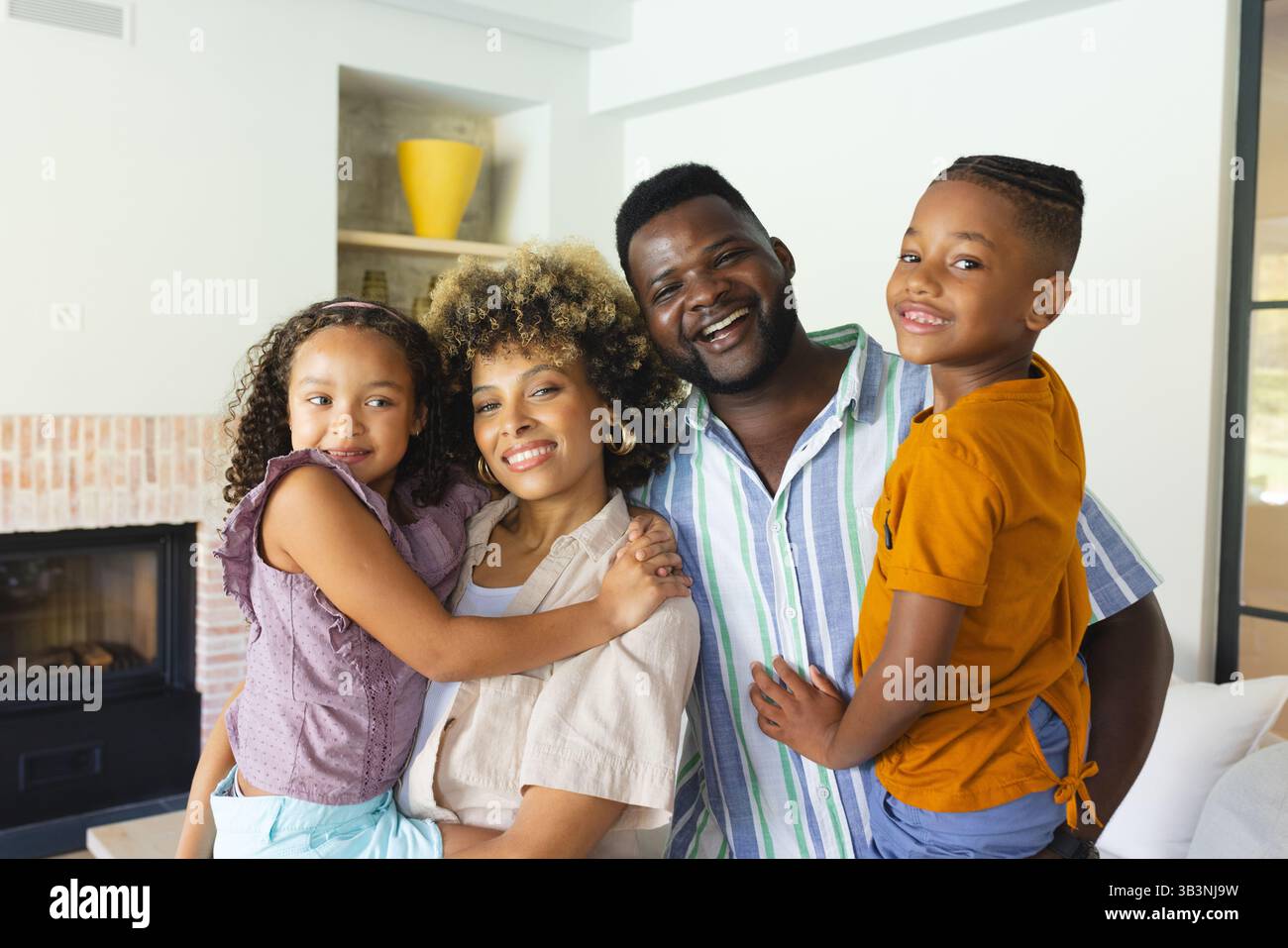Souriante famille embrassant dans le salon moderne lumineux, cheminée en brique et vase jaune Banque D'Images