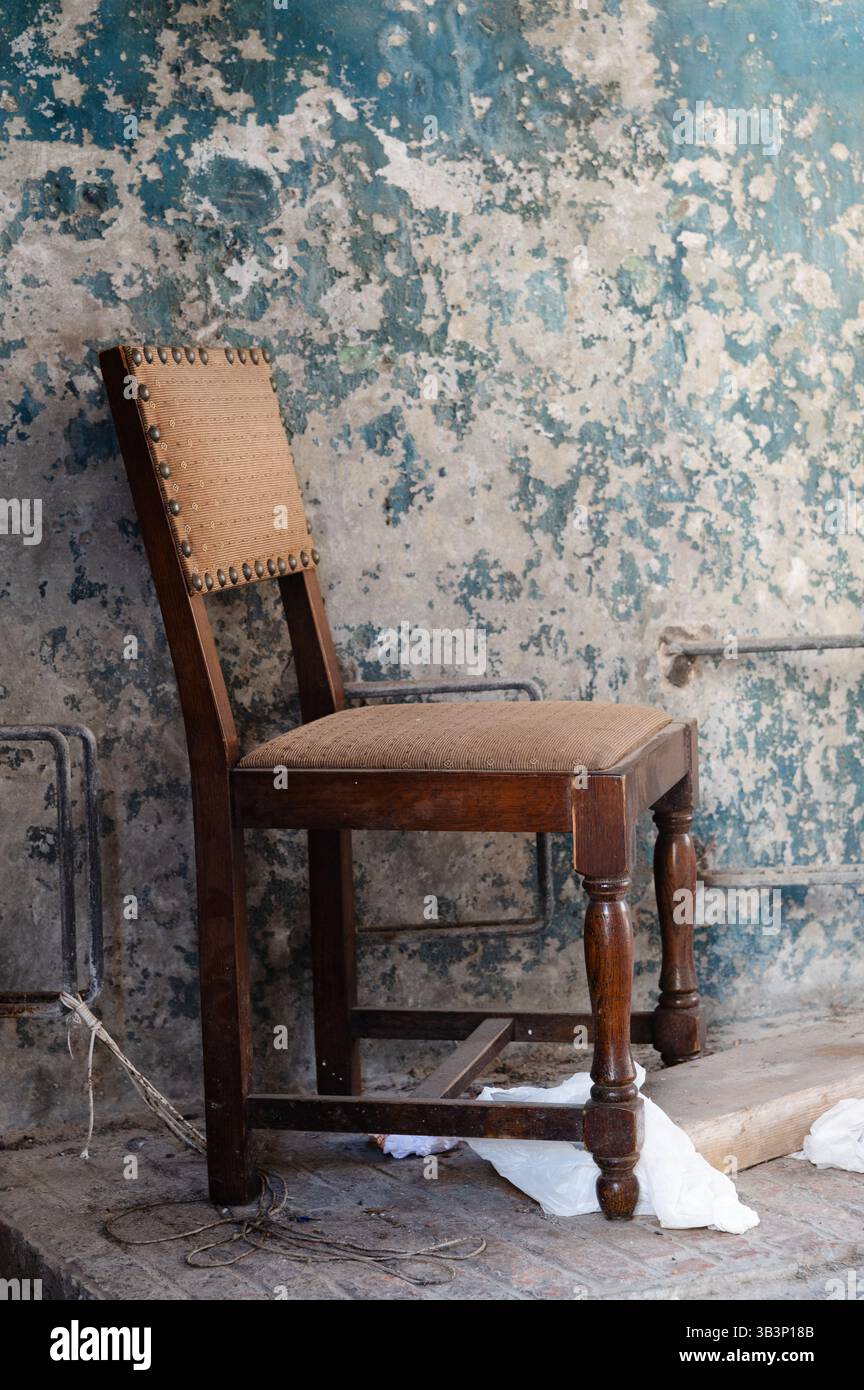 Une vieille chaise en bois se tient tranquillement contre un mur qui a de la peinture écaillée, mettant en valeur le passage du temps et l'usure dans sa composition Banque D'Images