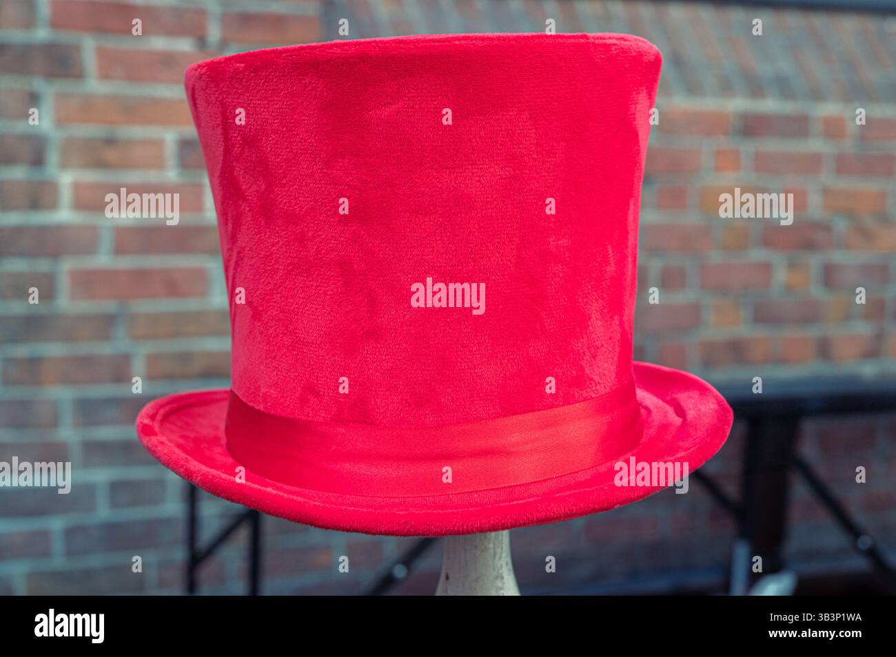 Un chapeau haut-de-forme rouge vif présenté sur un stand contre un mur de briques texturé, capturant l'essence de la mode classique avec une touche moderne et une couleur vibrante Banque D'Images