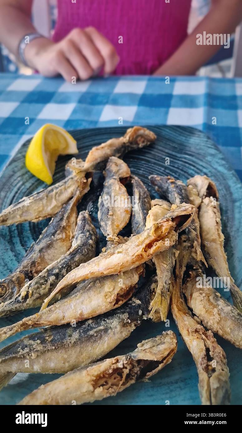 Gros plan assiette de poisson frit de maquereau cheval sur la table dans un restaurant et une femme pressant du jus de citron au-dessus, prêt à profiter du repas Banque D'Images