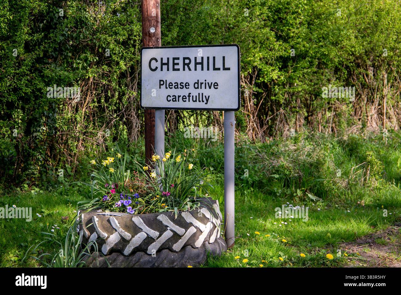 Un panneau routier à Cherhill, au Royaume-Uni, exhortant les conducteurs à conduire prudemment, entouré d'une végétation luxuriante et d'un planteur de pneus rempli de fleurs Banque D'Images