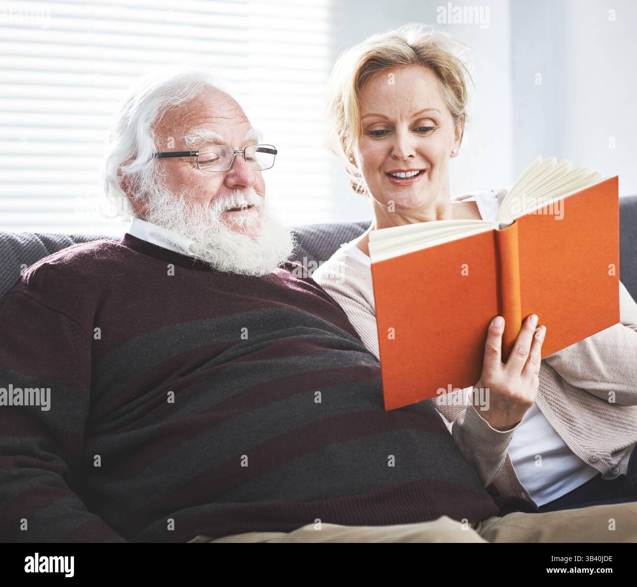 Heureux couple mature lisant un livre ensemble pendant les loisirs sur le canapé à la maison. Homme senior et femme appréciant la littérature classique, fiction ou non Banque D'Images