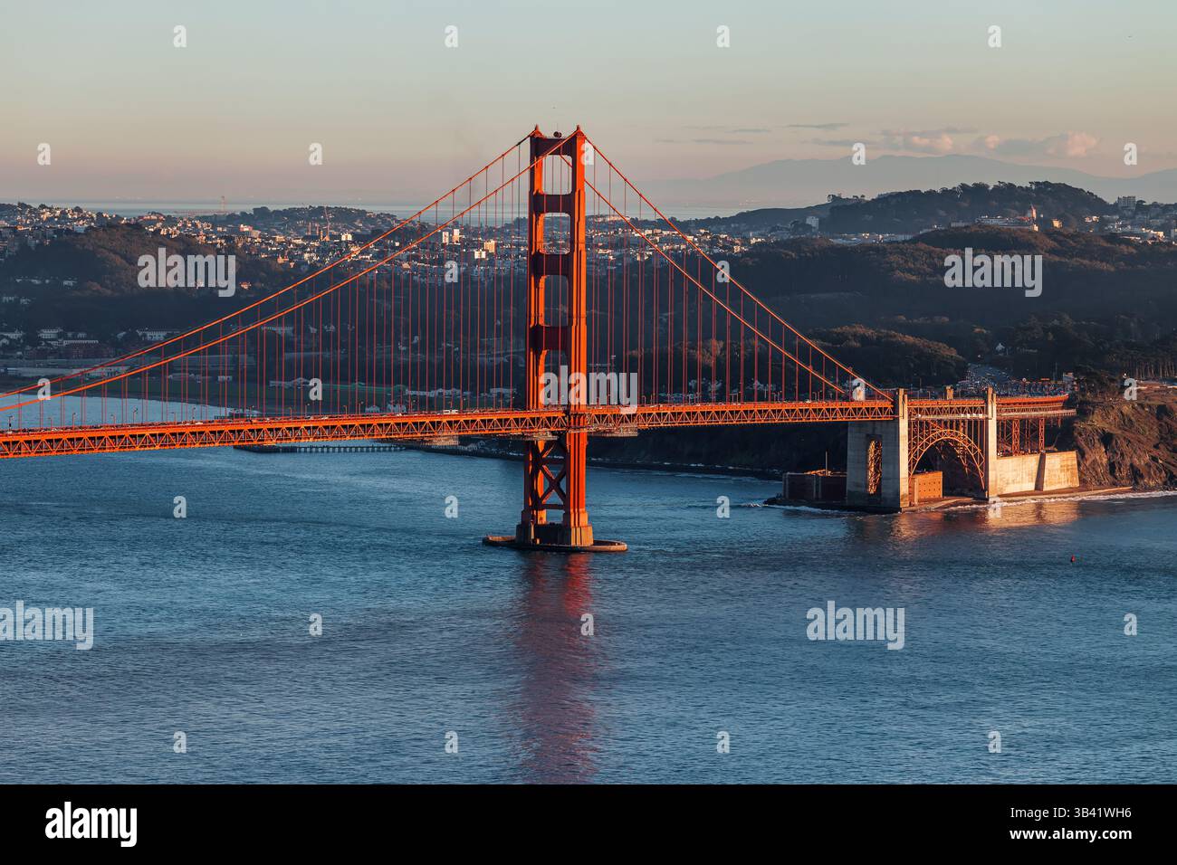 Le Golden Gate Bridge se dresse bien en vue au coucher du soleil, surplombant la baie de San Francisco avec un ciel dégagé et des collines lointaines Banque D'Images