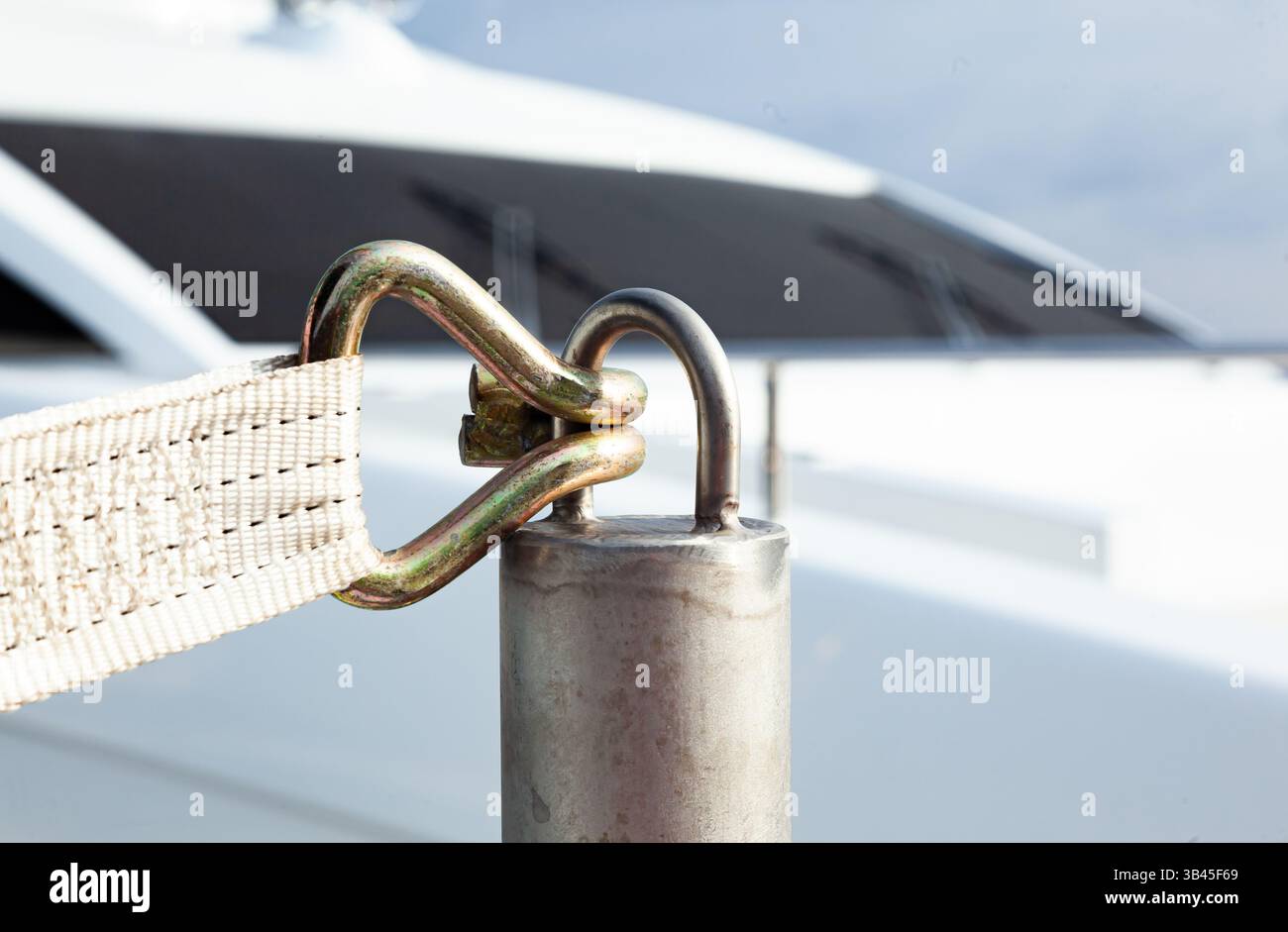 Une longe cargo avec un crochet à l'extrémité est fixée sur une entretoise en aluminium contre la toile de fond d'un yacht de luxe, gros plan. Banque D'Images