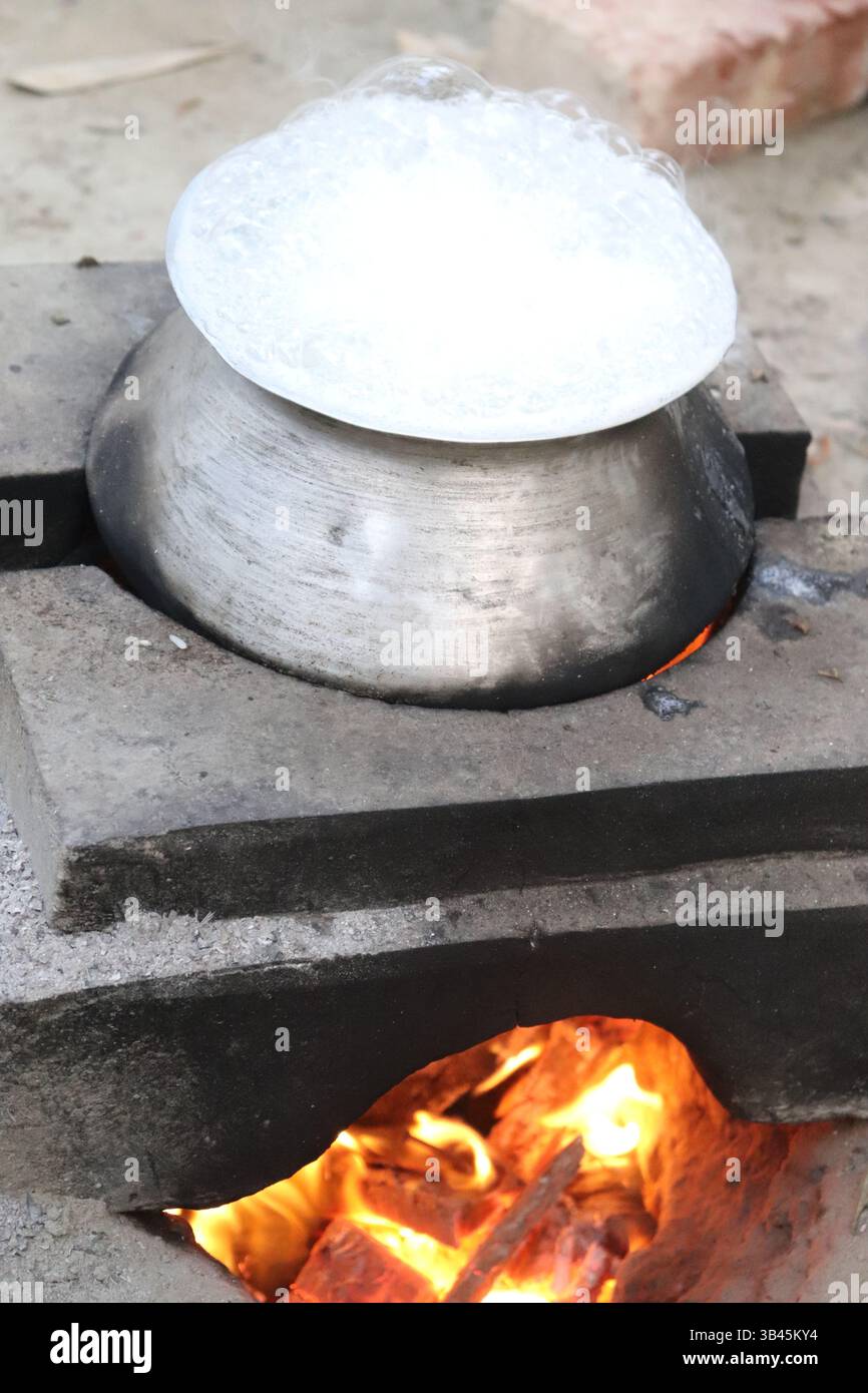 Le liquide bouillant déborde du pot métallique au sommet d'un feu ouvert sur des blocs de béton. La flamme allume la cuisinière traditionnelle. Banque D'Images