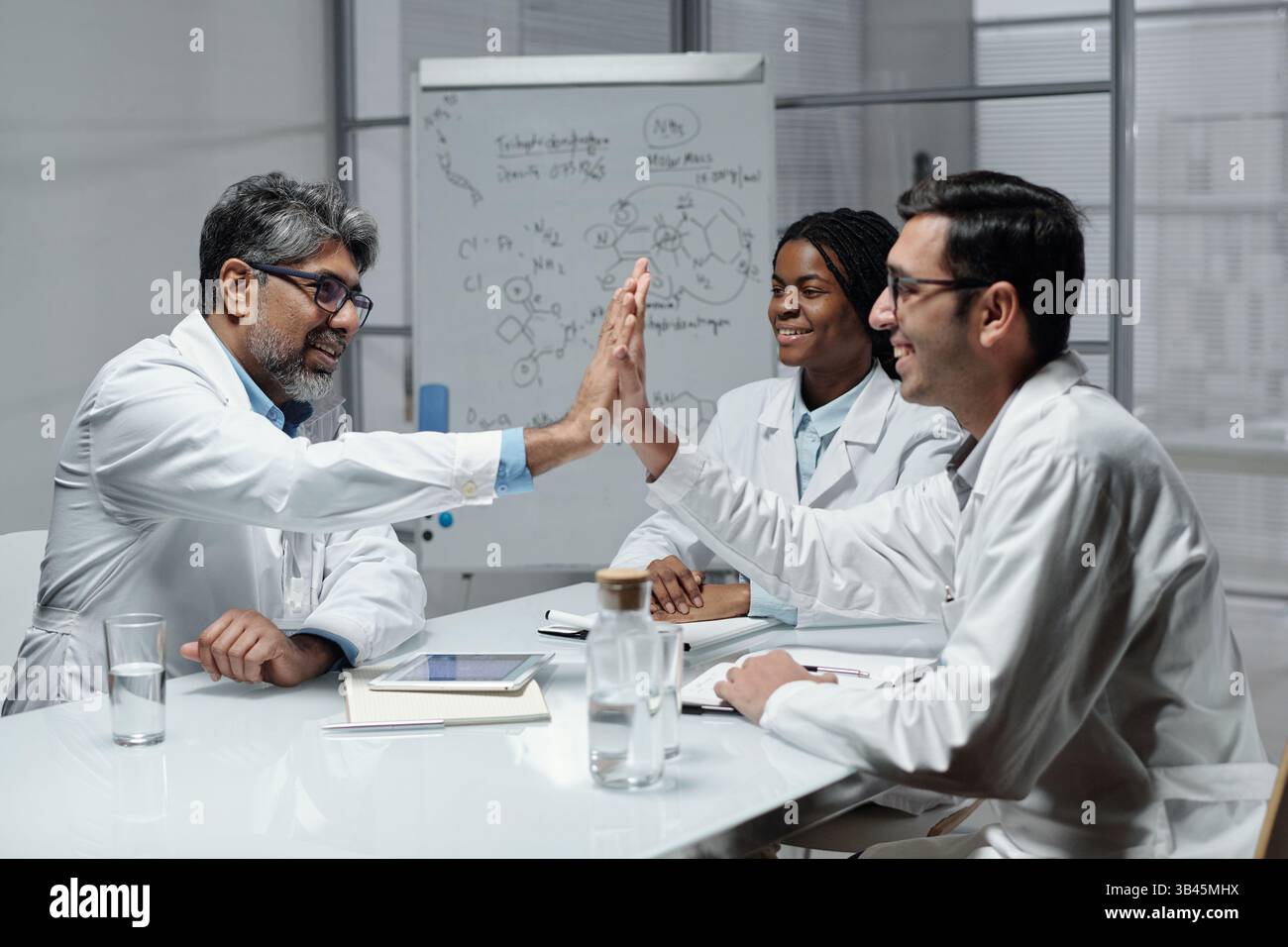 Groupe de scientifiques discutant des résultats de la recherche en laboratoire avec tableau blanc en arrière-plan et verre d'eau sur la table. Environnement engageant et collaboratif Banque D'Images