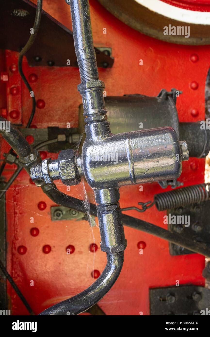 Un tuyau noir et argenté est attaché à une machine rouge et blanche. Le tuyau est recouvert d'une substance blanche, qui peut être de la rouille ou de la peinture. Le point d'accès de la machine Banque D'Images