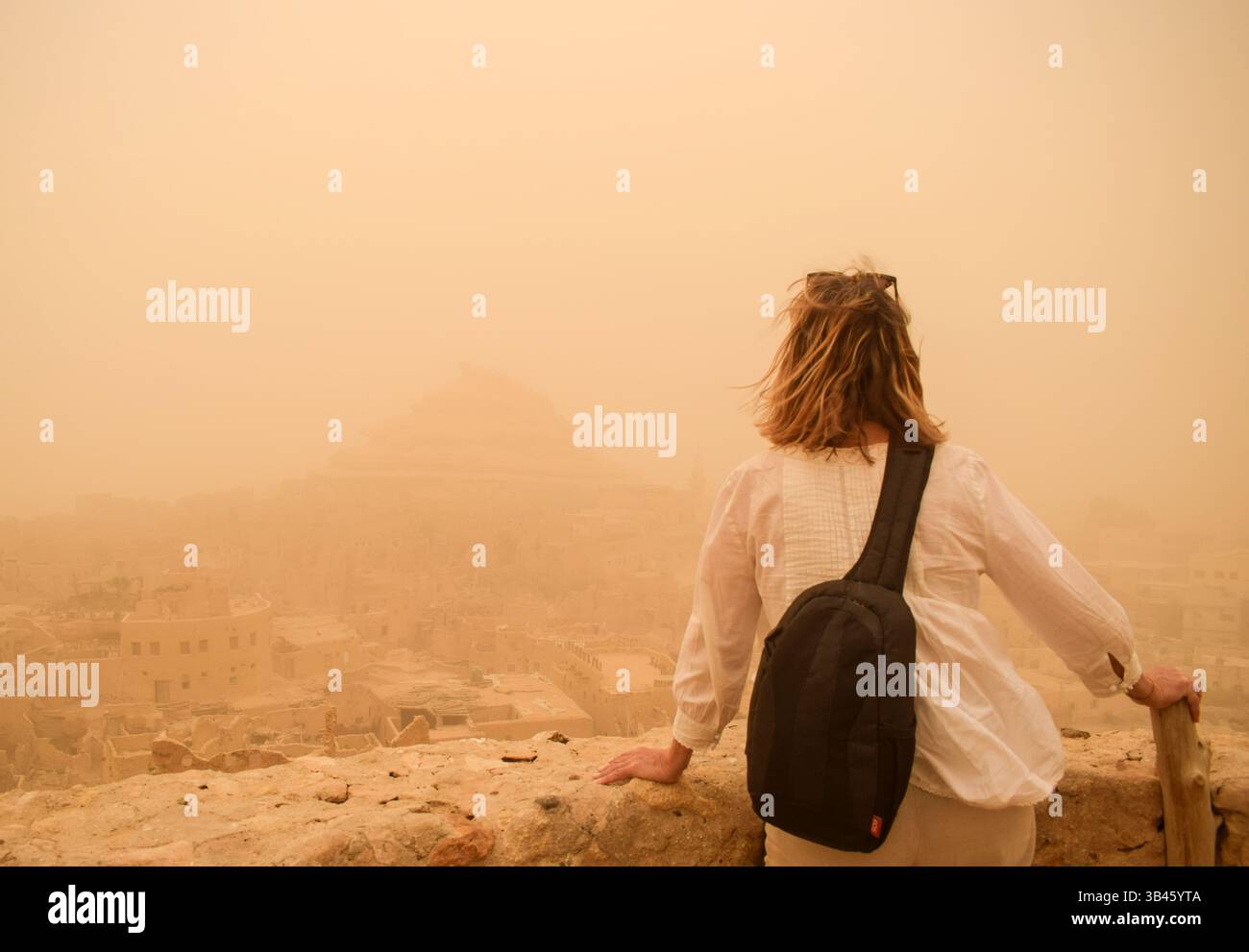 Oasis de Siwa, Égypte, 29 avril 2025. Un visiteur regarde la vieille ville de l'oasis de Siwa alors qu'elle est couverte d'un nuage orange de poussière du Sahara en raison d'une tempête Khamsin. L’Égypte a émis une alerte météo à la suite d’une violente tempête Khamsin et ferme des écoles dans tout le pays mercredi. Crédit : Dimitris Aspiotis/Alamy Live News Banque D'Images