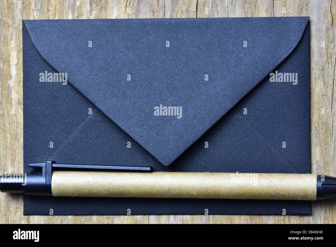 Petite enveloppe noire sur fond bois et stylo durable en papier recyclé. Lettre minimaliste. Banque D'Images