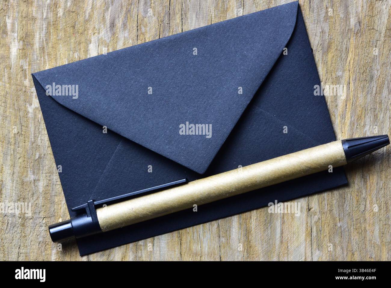 Petite enveloppe noire sur fond bois et stylo durable en papier recyclé. Lettre minimaliste. Banque D'Images