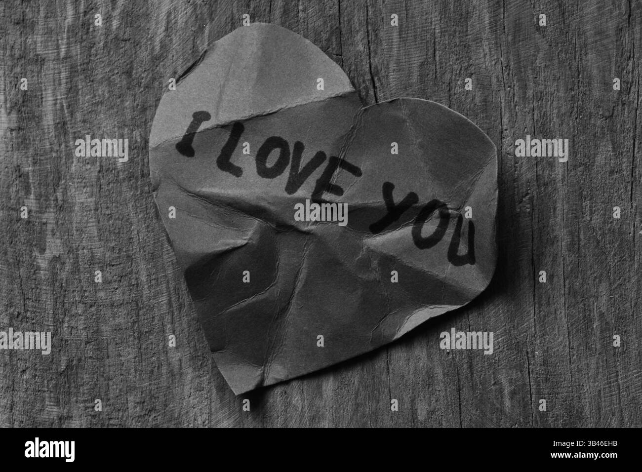 Texte du message je t'aime sur la carte de papier en forme de coeur froissé pour la Saint-Valentin sur fond texturé de planche de bois. Carte de Saint-Valentin cassée avec baguette Banque D'Images