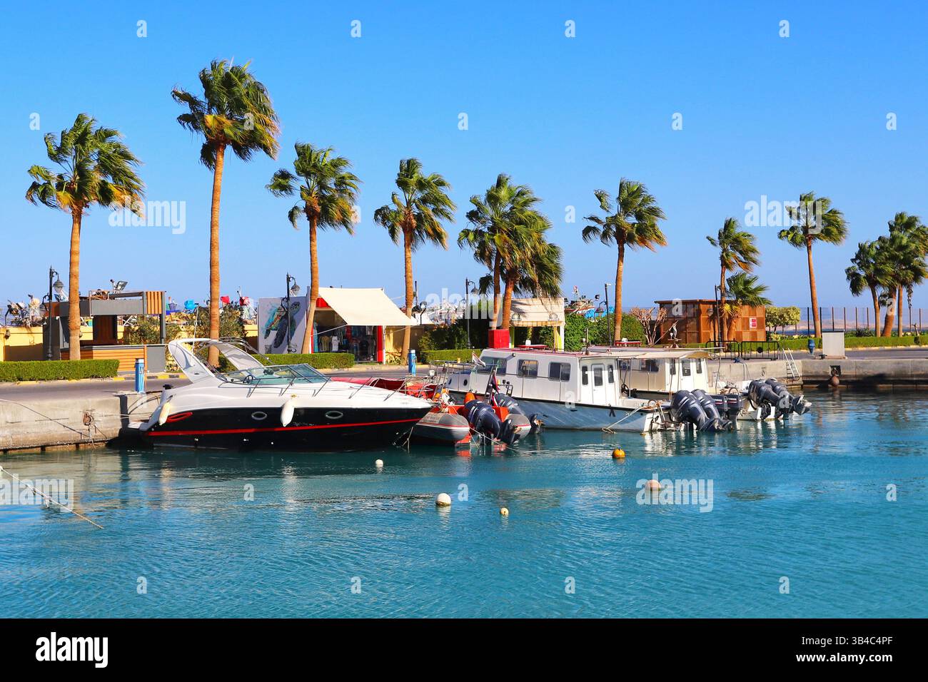 Yachts de luxe dans la marina à Hurghada, en Égypte, avec minarets mosquée et promenade bordée de palmiers sous un ciel bleu clair, scène de station balnéaire de la mer Rouge. Banque D'Images