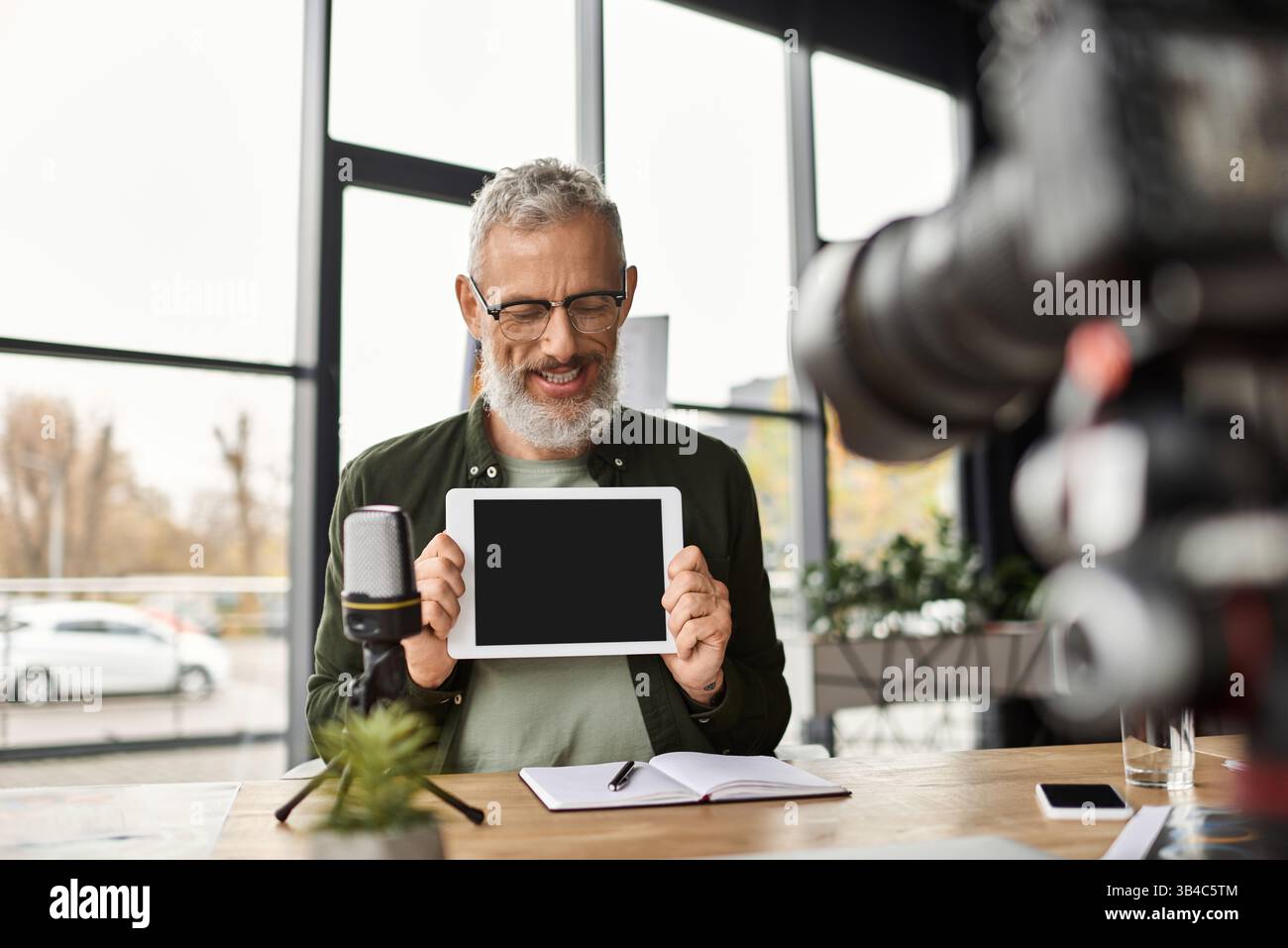 Un présentateur confiant présente une tablette tout en préparant des notes dans un environnement de bureau élégant. Banque D'Images