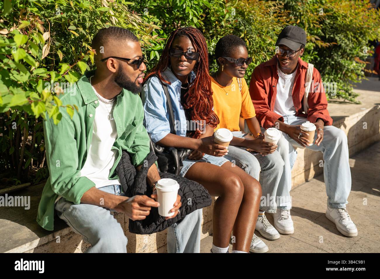 Groupe animé d'amis d'université afro-américains appréciant la conversation avec des boissons à emporter dans le parc Banque D'Images