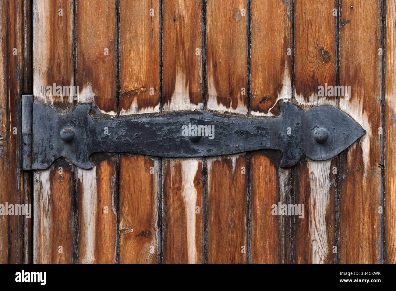 Vue détaillée d'une porte en bois vieilli avec une charnière en fer forgé noir ornée, présentant des textures, des motifs et un savoir-faire représentatif de Banque D'Images