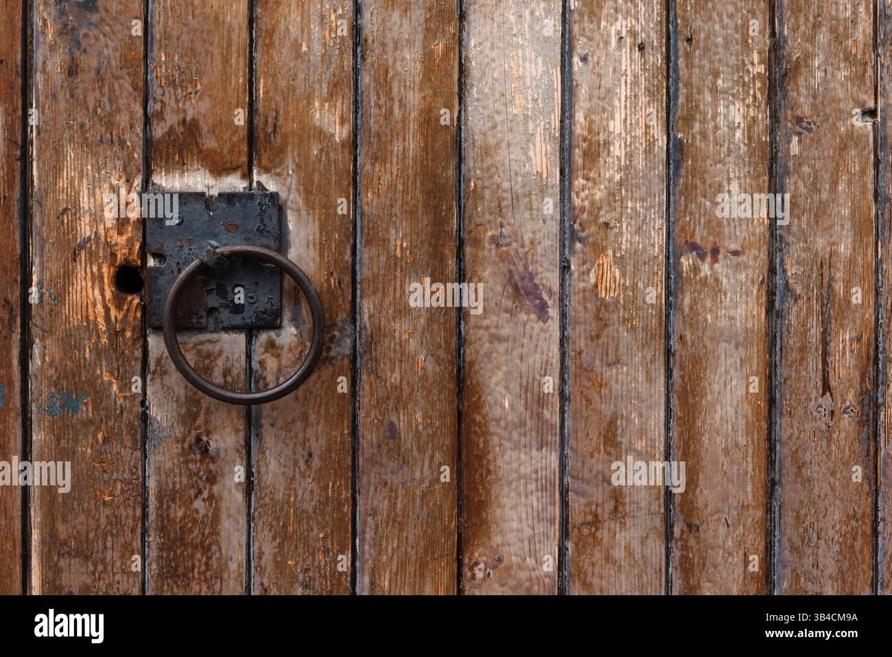 Gros plan d'une porte en bois vieilli avec une poignée annulaire en métal et un charme rustique altéré, évoquant un design architectural vintage et historique Banque D'Images