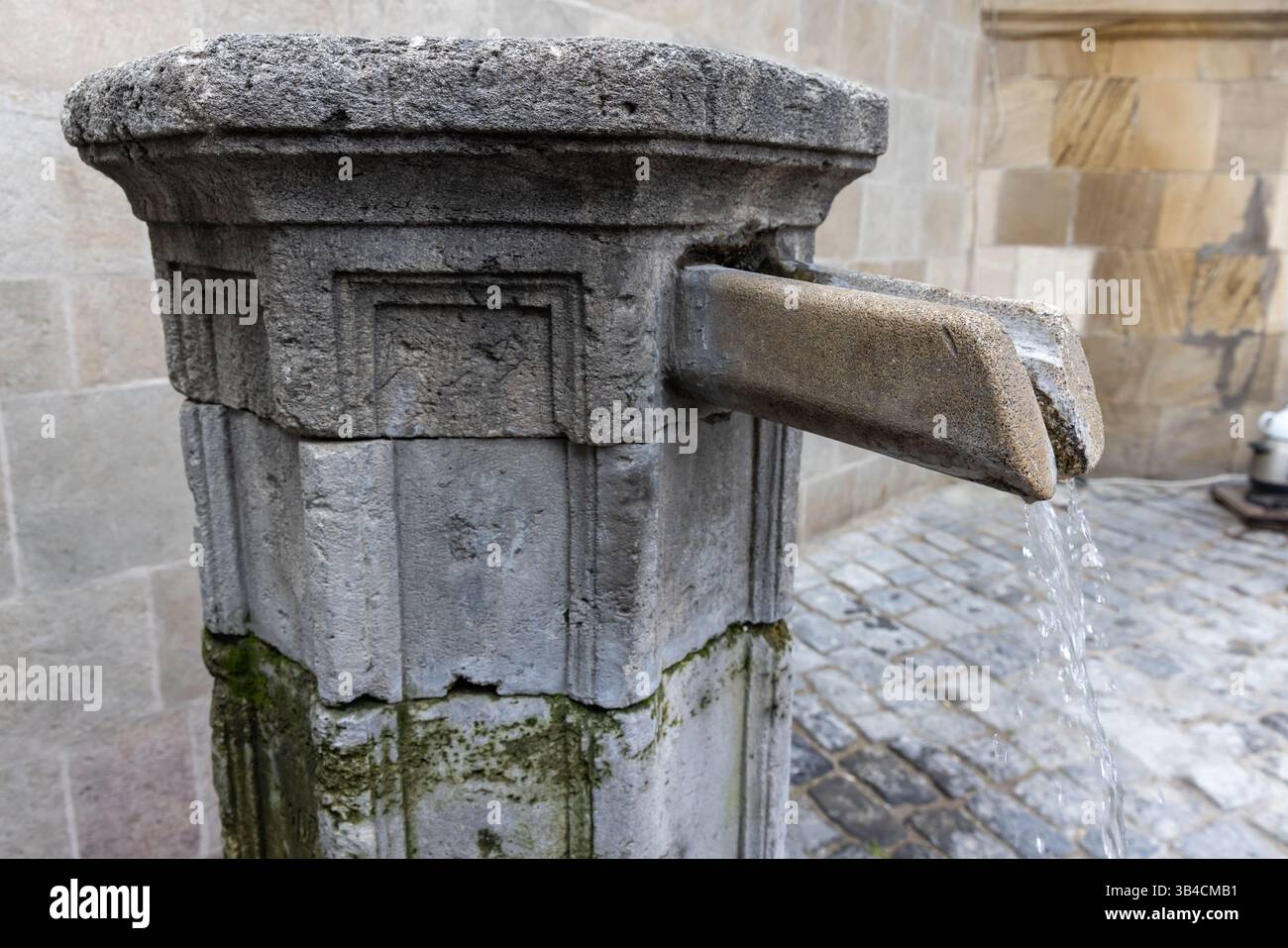 Scène rustique d'une vieille fontaine en pierre coulant avec de l'eau, situé contre un environnement urbain pavé. Bakou, Azerbaïdjan Banque D'Images