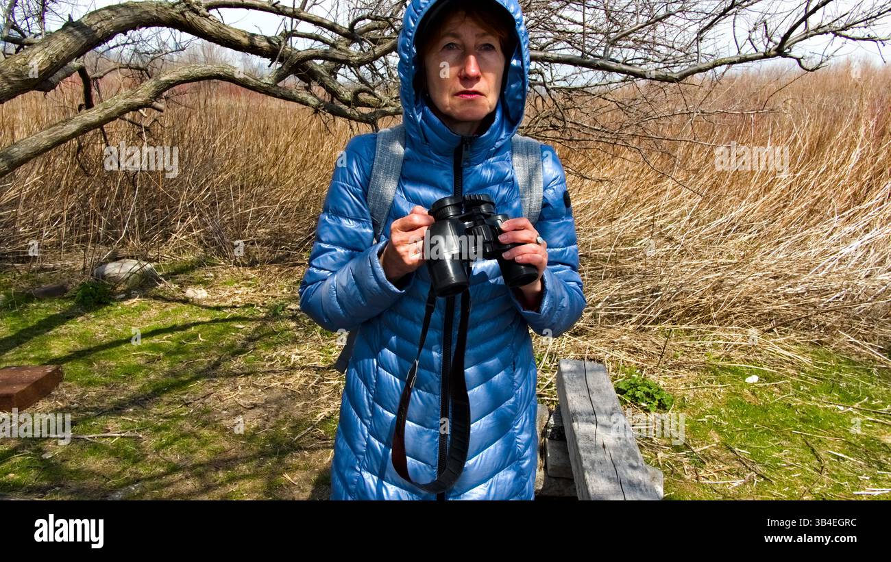 Une femme passionnée de plein air observe tranquillement à travers des jumelles dans un paysage rustique, embrassant le rythme des natures. Banque D'Images