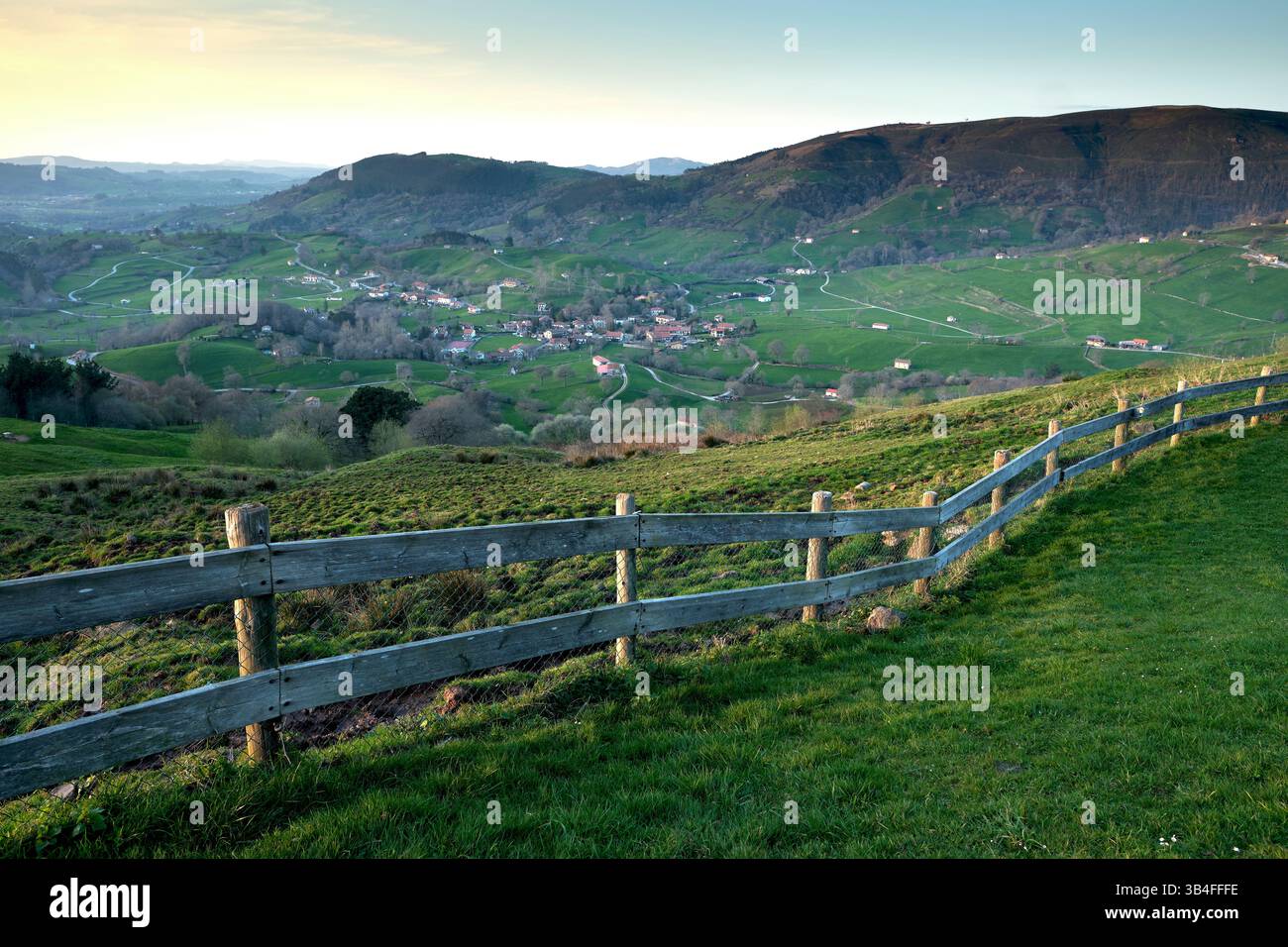 Vue imprenable sur une vallée paisible avec un petit village niché parmi des champs verdoyants, des montagnes, et une clôture en bois au premier plan. Esles, santa Banque D'Images