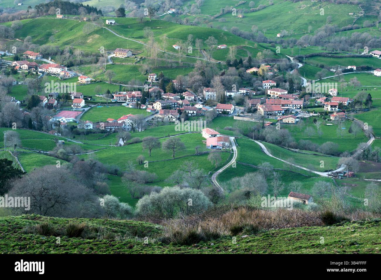 Des routes sinueuses traversent des champs verdoyants, reliant des maisons dispersées et des fermes dans une vallée sereine, mettant en valeur la beauté de la vie rurale. Esles, san Banque D'Images