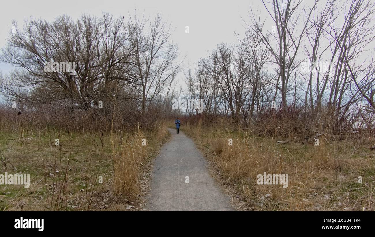 Une aventurière en solo vêtue d'un manteau bleu et de gants regarde à travers des jumelles tout en explorant un habitat naturel intact. Banque D'Images