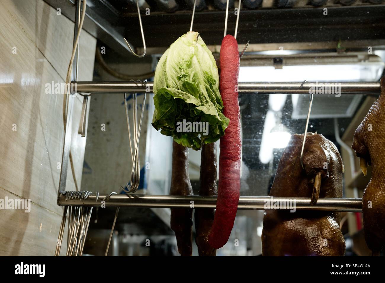 Des paires inhabituelles sont accrochées à la fenêtre d'un restaurant de Hong Kong : laitue, saucisse et canard rôti côte à côte Banque D'Images