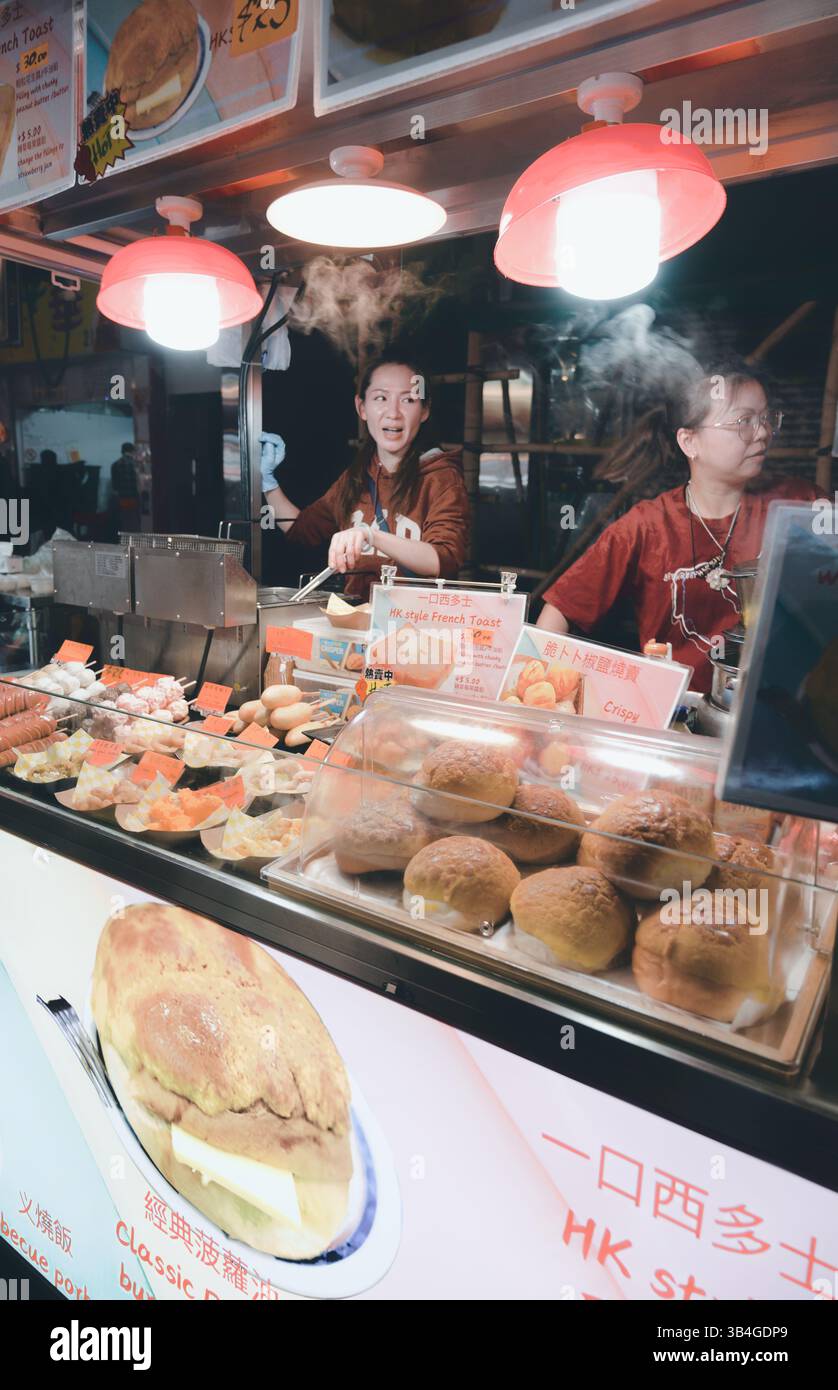 Les vendeurs servent du pain grillé et des petits pains à la vapeur de style HK sous les lumières du marché Banque D'Images