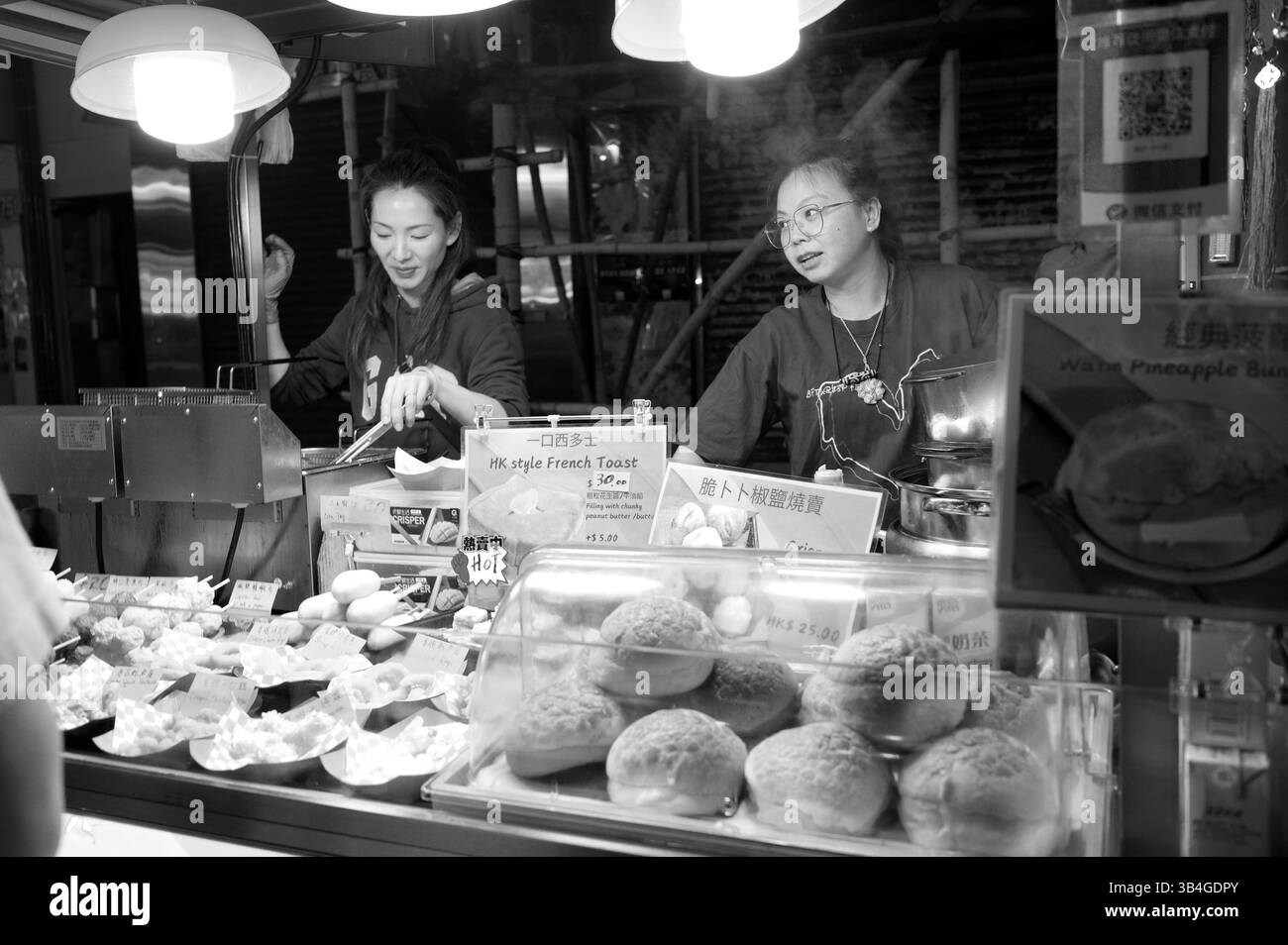 Hong Kong - 2 février 2025 - vendeurs joyeux servant des petits pains de style HK et des toasts sous des lumières vives Banque D'Images