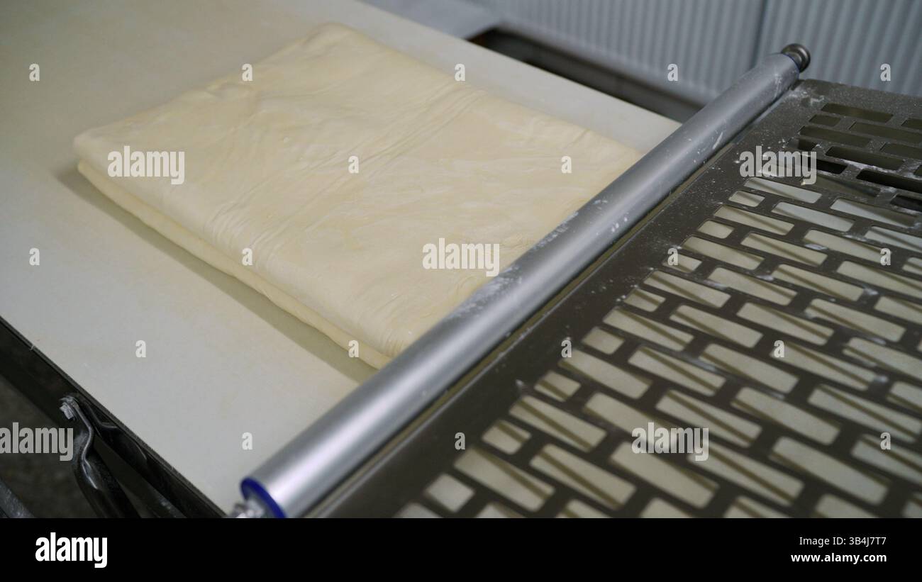 Feuille de pâte feuilletée et rouleau à pâtisserie reposant sur une table en acier inoxydable dans une boulangerie ou une usine alimentaire Banque D'Images