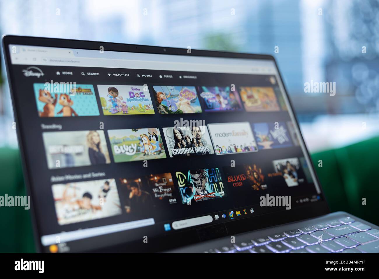 Bucarest, Roumanie - 30 juillet 2024 - ordinateur portable montrant la plate-forme de streaming de page Web Disney plus utilisée par un homme pour regarder et se détendre dans son bureau personnel. Jeune PDG binge regardant sur le canapé. Banque D'Images